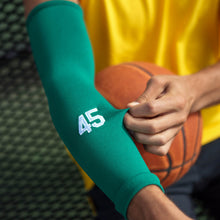 Load image into Gallery viewer, A closeup of an arm sleeve on a basketball player&#39;s arm while he sits on a park bench. The sleeve has the number 45 on it, and the player is tugging the stretchy material.
